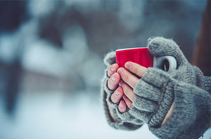 Hände umschließen eine dampfende Tasse Tee im Winter