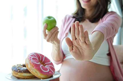 Schwangere lehnt Donuts ab und hält Apfel in der Hand