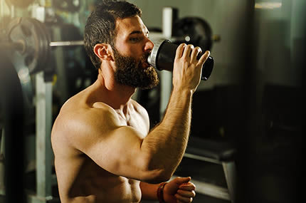 Sportler mit Bart trinkt Shake im Fitnessstudio zur Regeneration