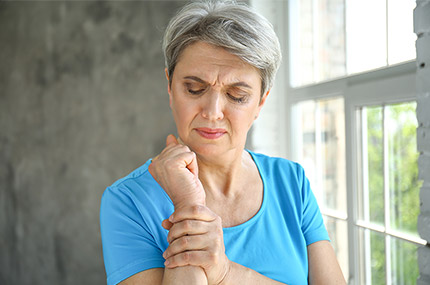 Frau hält ihren schmerzenden Arm, Zeichen einer rheumatoiden Arthritis