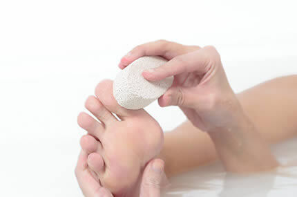 Füße werden mit einem Bimsstein gepflegt, um Hornhaut und Fußprobleme vorzubeugen