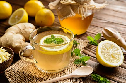 Glas-Teetasse mit Ingwertee, Honig, frischem Ingwer und Zitrone daneben