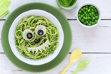 Teller mit grünen Spaghetti und Monster-Gesicht aus Ei und Olive, daneben Erbsen