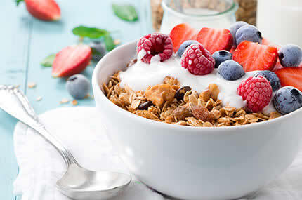 Schale mit Müsli, frischen Beeren und Joghurt auf hellem Tisch